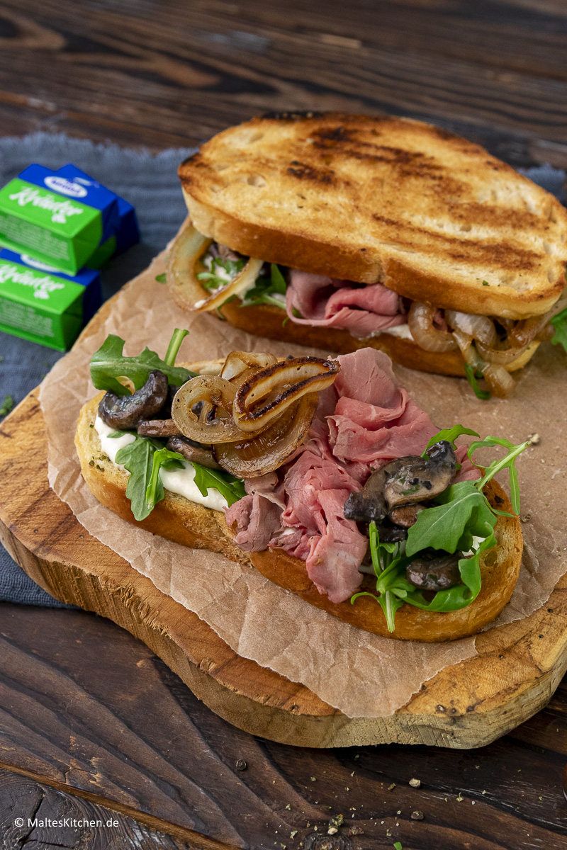 Gegrilltes Roastbeef-Sandwich mit Kräuterbutter-Champignons, gegrillten zwiebeln und Honig-Senf-Sauce.