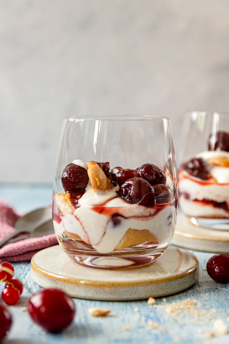 Dessert mit Joghurt, Kirschen und Biskuitzungen.