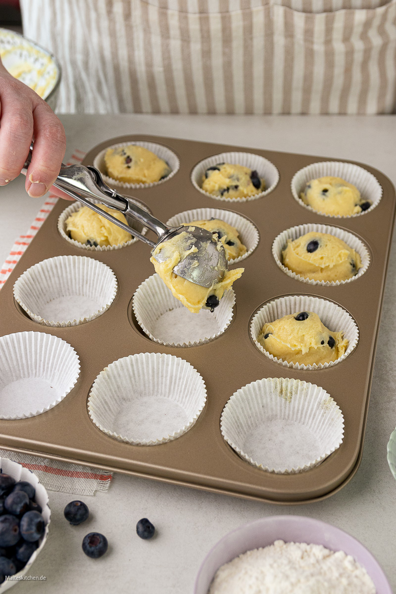 Muffins Teig wird in Papierförmchen gefüllt.